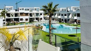 Een modern hotel met een zwembad, palmbomen en een helderblauwe lucht.