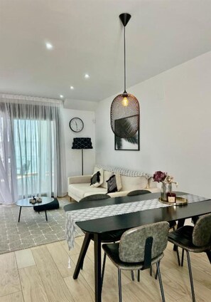 A modern living room with a sofa, dining table, chairs, a hanging light fixture, and a large window with sheer curtains. - Condo with solarium in Laguna Beach Resort In Los Balcones in Torrevieja (Torrevieja)