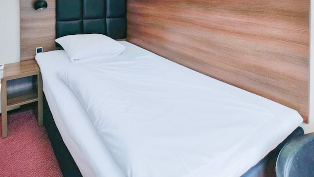 Ein Einzelbett mit Holz Kopfteil, weißer Bettwäsche, einem Nachttisch und einem roten Teppich.