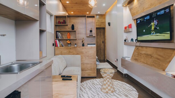 A modern kitchen with a built-in island, wooden ceiling, recessed lighting, and a flat-screen TV mounted on the wall. - Misteph Luxury Living (Kigali)