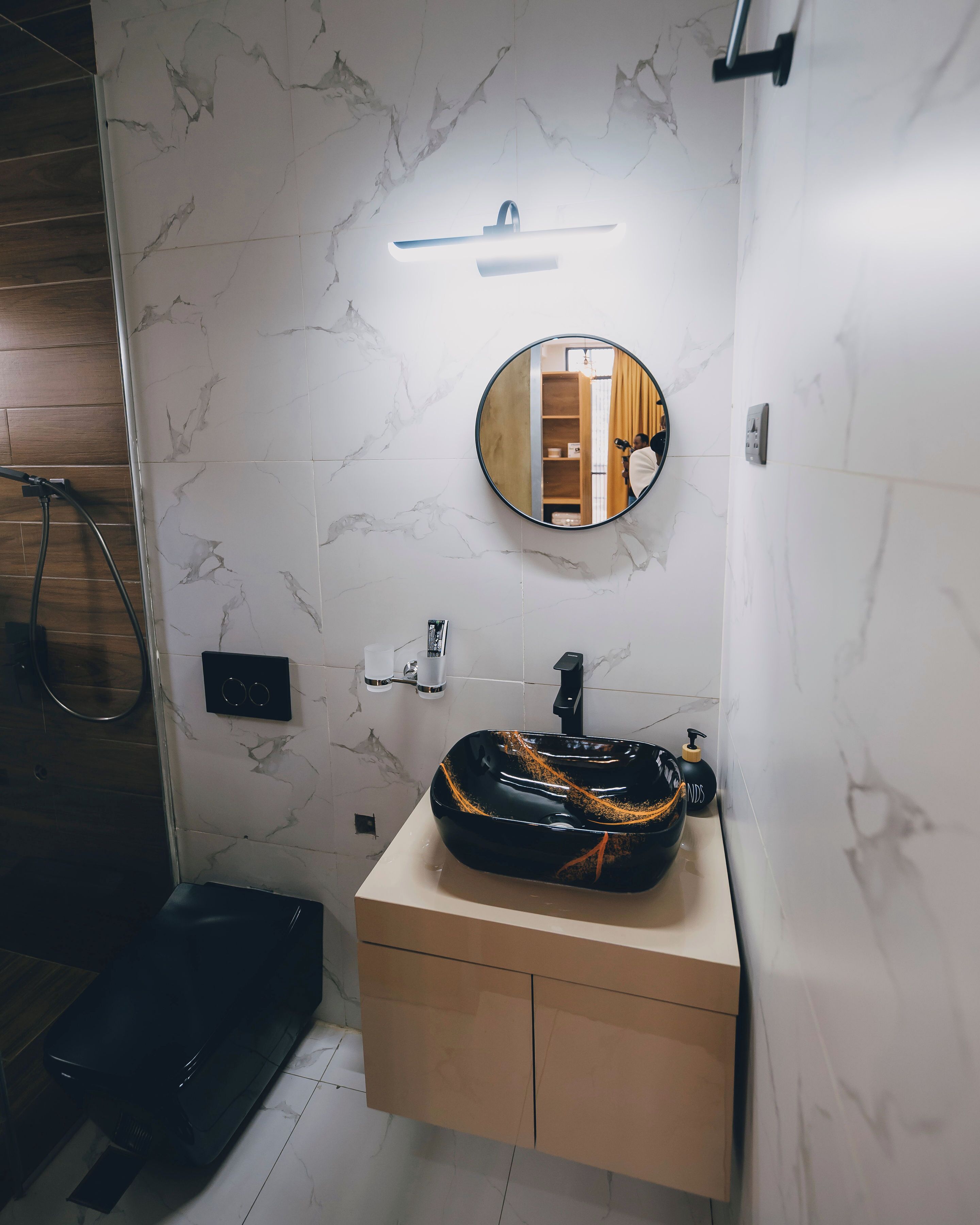 Un baño con pared de mármol, un espejo redondo, un lavabo negro y un mueble de madera.