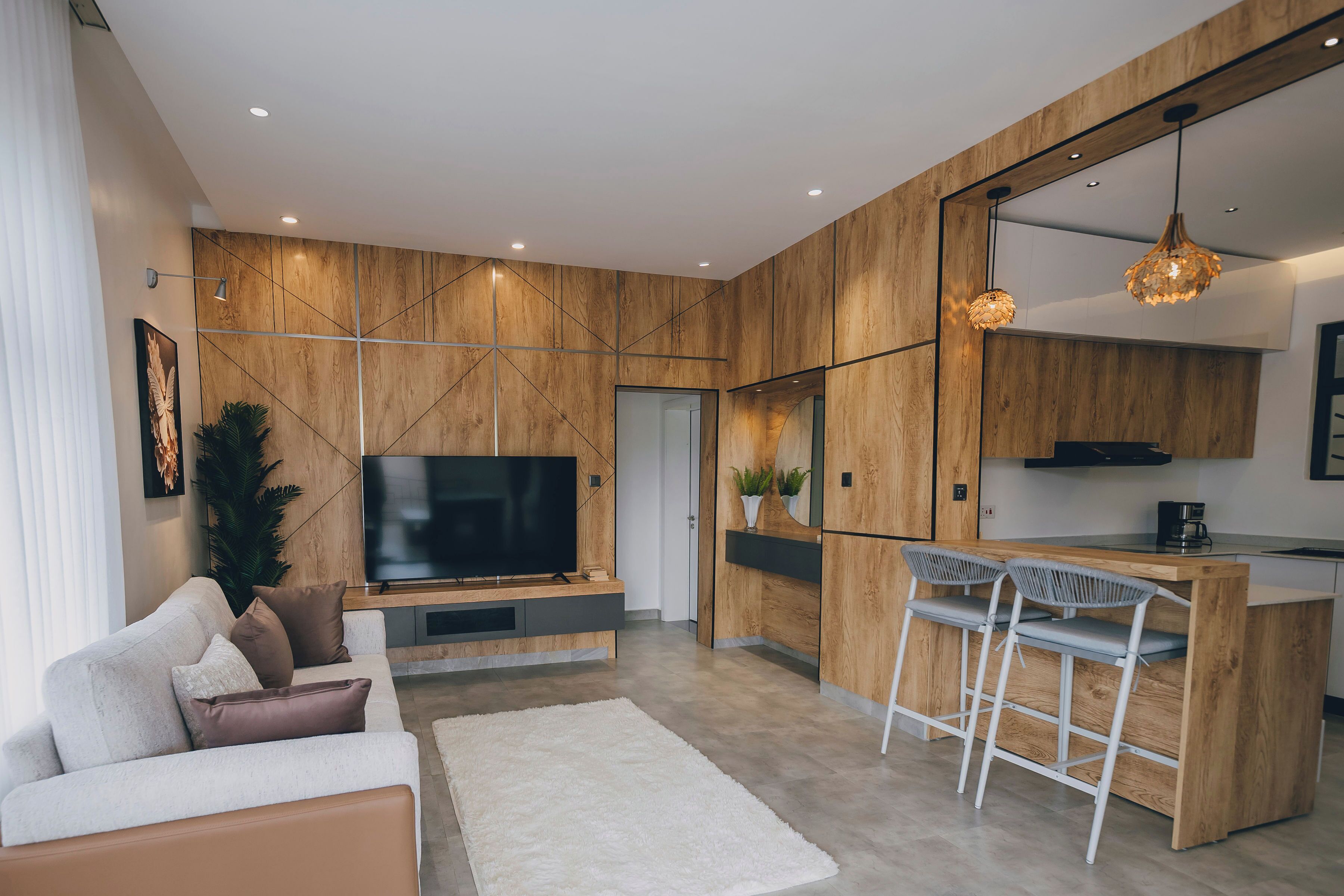A modern living room with a flat-screen TV, a sofa, a coffee table, and a bar area with bar stools.