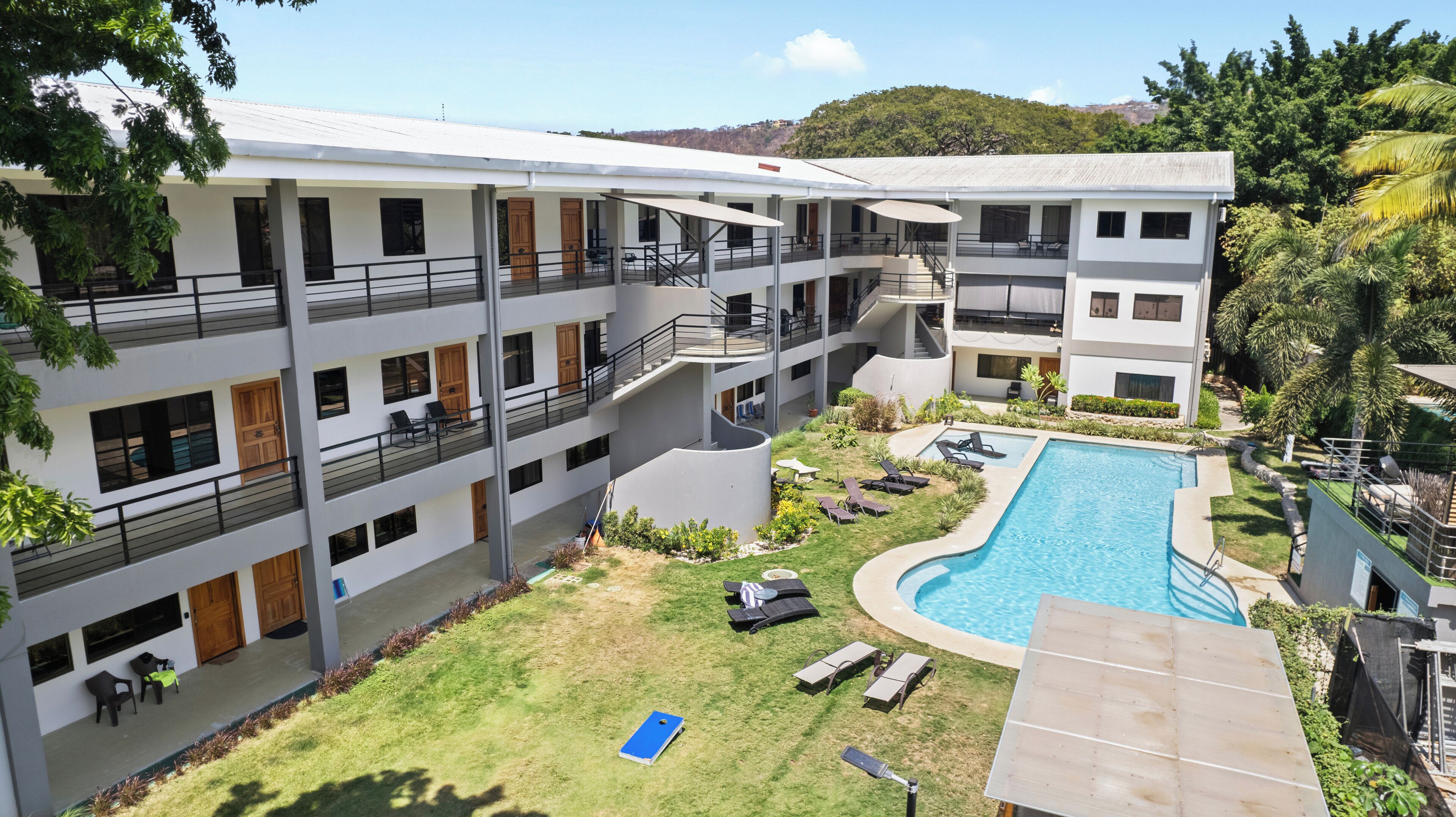 Un hotel de varios pisos con piscina, mobiliario exterior y un jardín exuberante.