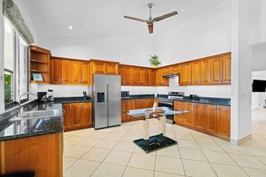 Eine moderne Küche mit Holzschränken, Edelstahlgeräten, einer Glasinsel und einem Deckenventilator.