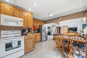 A kitchen with wooden cabinets, a microwave, stove, refrigerator, and a dining area with chairs and a table. - Bearitage Chalet Family Poconos Retreat in The Hideout Lake Pool Ski (The Hideout)