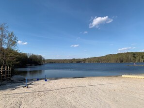 A sandy beach with a clear blue sky, a calm lake, and a forested hill in the background. - Bearitage Chalet Family Poconos Retreat in The Hideout Lake Pool Ski (The Hideout)