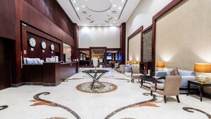 A hotel lobby with a reception desk, seating area, and a large screen. - Taleen Serviced Apartments Granada (Riyadh)