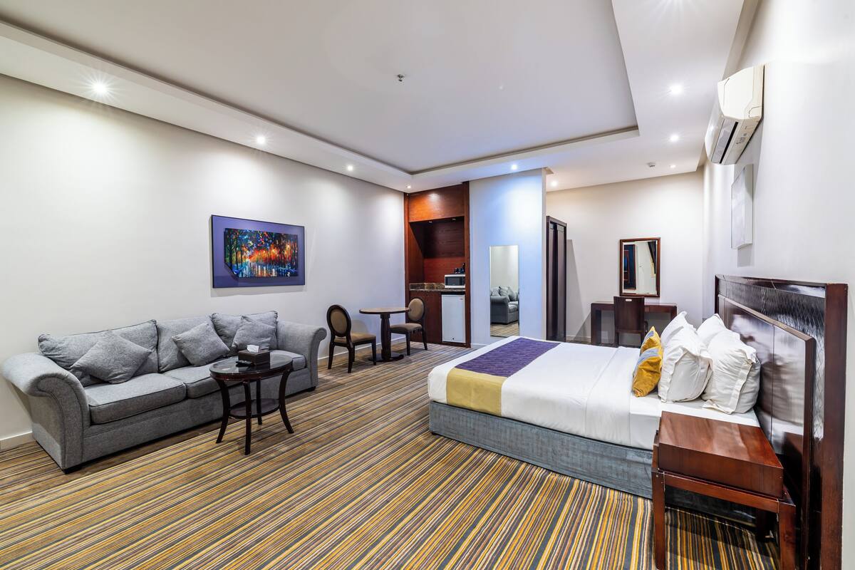 Quarto de hotel com cama, sofá, mesa pequena e escrivaninha.