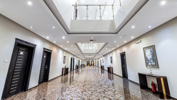 A hotel hallway with a reflective marble floor, black doors, and a ceiling with recessed lighting. - Taleen Serviced Apartments Granada (Riyadh)
