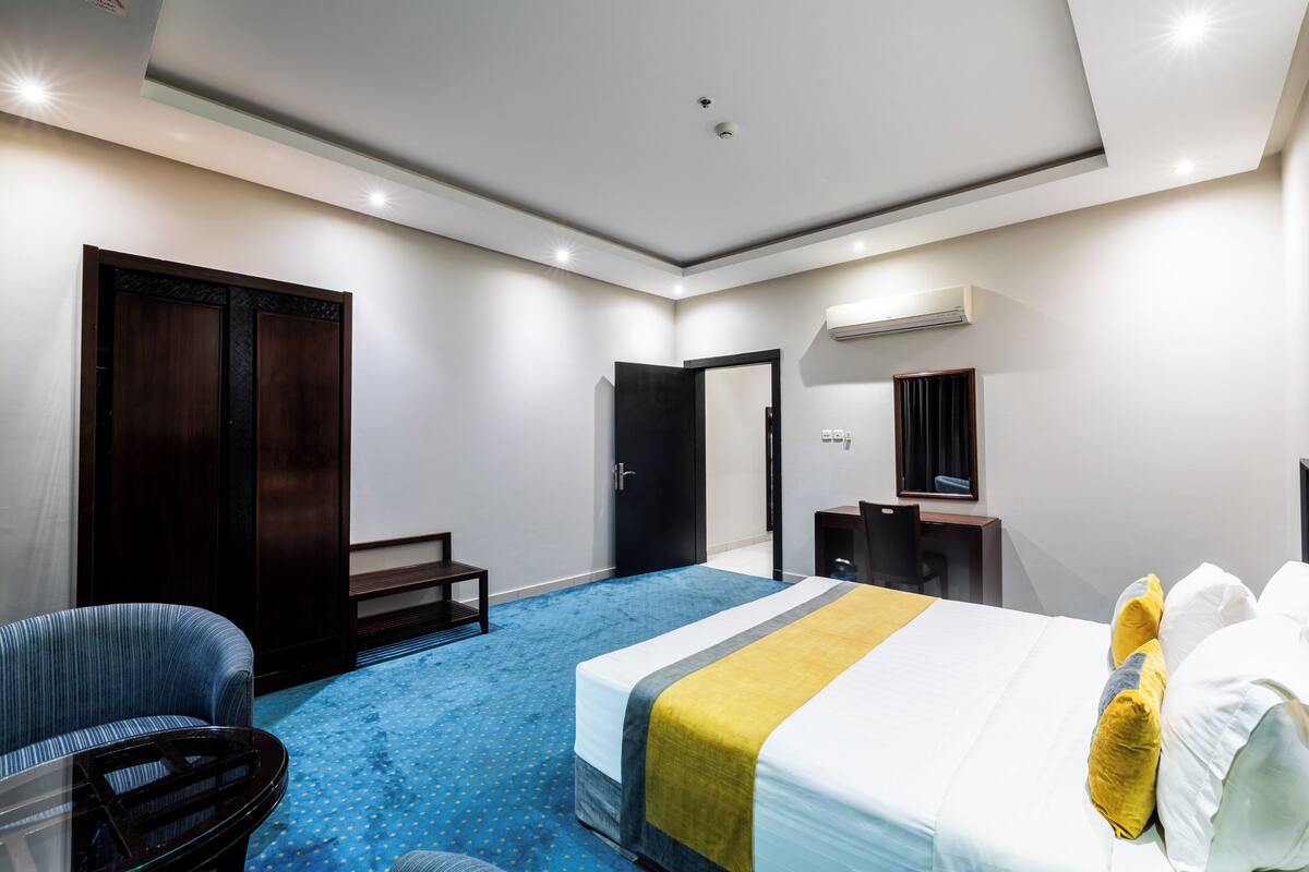Quarto de hotel com cama, escrivaninha, cadeira, guarda-roupa e espelho.