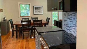 Una cocina moderna con comedor, sillas de madera, estufa negra y ventana con vista a árboles.