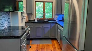 Una cocina moderna con armarios grises, un refrigerador de acero inoxidable y una ventana con vista a zonas verdes.