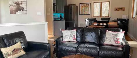 Una sala de estar con un sofá de cuero negro, una mesa de centro de madera y un comedor con una mesa y sillas.