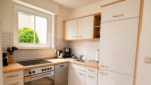 Une cuisine de taille réduite, dotée d’une fenêtre, d’une cuisinière, d’un lave-vaisselle et de meubles de couleur claire.
