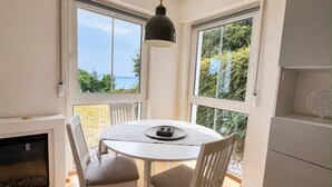 Un coin repas comprenant une table ronde, deux chaises, un luminaire suspendu et une vue sur l’extérieur grâce à de grandes fenêtres.