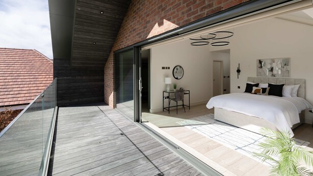 A modern bedroom with a large bed, a glass door leading to a balcony, and a brick wall. - Woldside - Luxury Property Sleeps 10 (York)