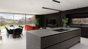 A modern kitchen with a large island, a dining area with a table and chairs, and a large window with a view of the countryside. - Woldside - Luxury Property Sleeps 10 (York)