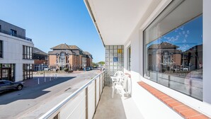 Ein Balkon mit Blick auf eine Straße, ein Gebäude mit traditioneller Fassade und ein modernes Gebäude mit großen Fenstern.