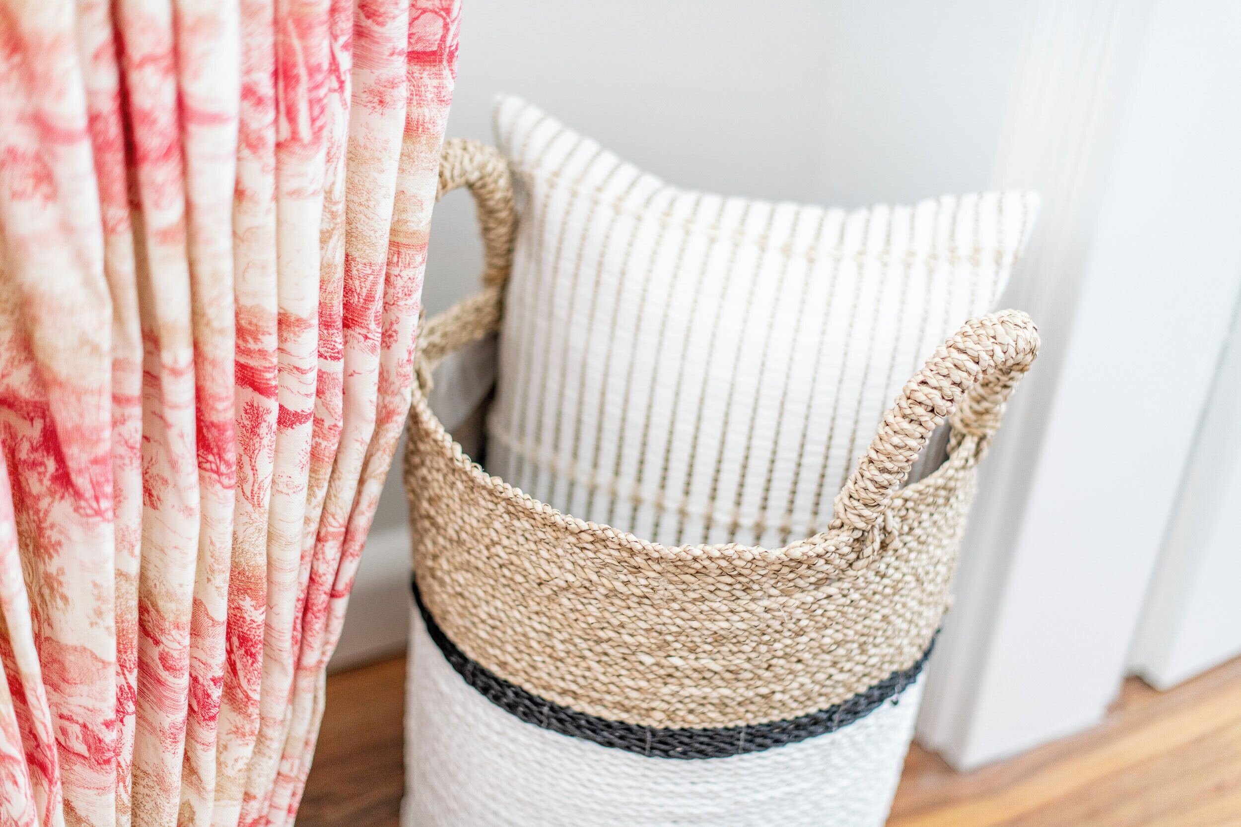 A woven basket with a handle, a striped cushion, and a curtain with a red and white pattern.
