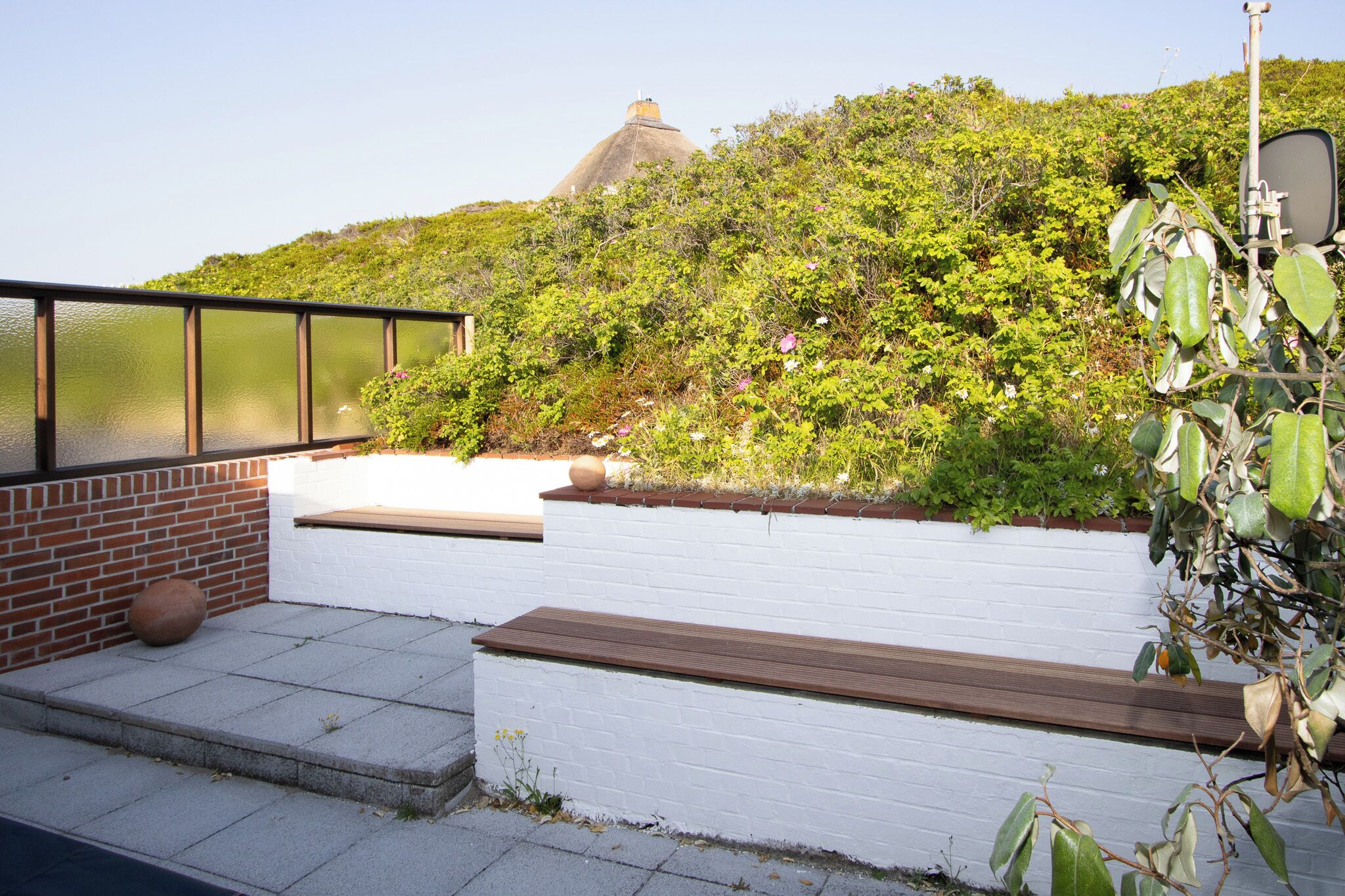 A patio with a white wall, a wooden bench, and a brick wall.