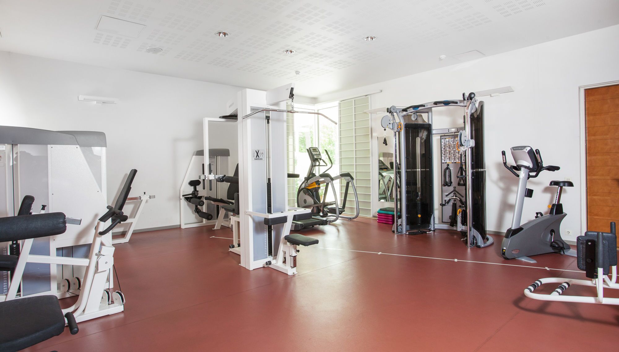 Un gimnasio con diversas máquinas de ejercicio, un espejo grande y una puerta que da a otra habitación.