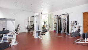 A gym with various exercise machines, a mirrored wall, and a door leading to another room.