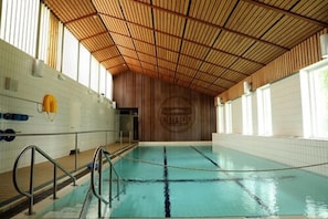 Ein Hallenbad mit Holzbalkendecke, gefliesten Wänden und einem Rettungsschwimmerstuhl.