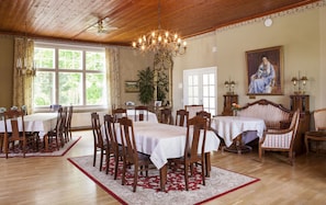 Ein Esszimmer mit Holztischen, Stühlen, einer Chandelier und einem großen Fenster mit Vorhängen.