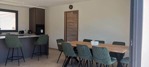 Ein moderner Essbereich mit Holztisch und grünen Stühlen, einer Küchenarbeitsplatte mit Barhocker und einem großen Fenster.