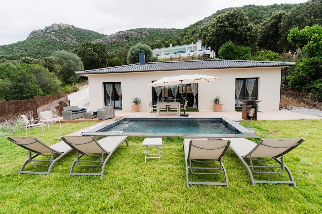 Une maison moderne dotée d’une piscine, d’un espace extérieur aménagé et offrant une vue sur un paysage montagneux.