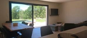 Ein modernes Wohnzimmer mit Essbereich, großen Schiebeglastüren zum Garten und einem wandmontierten Flachbildfernseher.