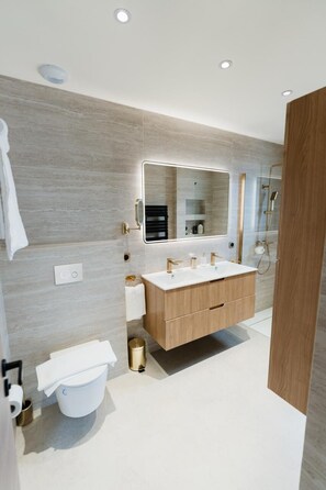 Une salle de bain moderne avec un grand miroir, des toilettes blanches, un meuble-lavabo en bois et un espace douche.