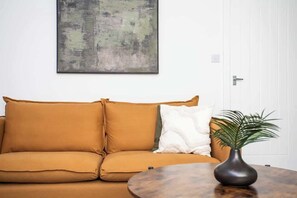 A room with a sofa, a round table, a plant, and a painting on the wall.