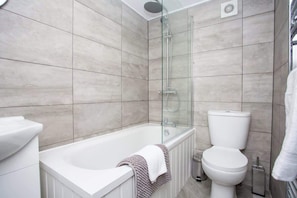 A modern bathroom with a glass-enclosed shower, a white bathtub, and a toilet.