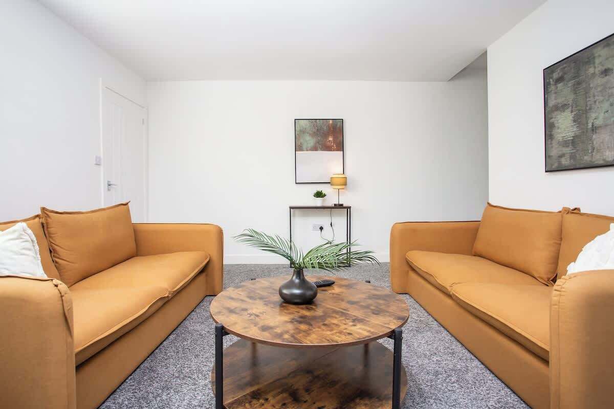 Una habitación con dos sofás, una mesita de centro redonda, una planta en maceta y dos cuadros en la pared.
