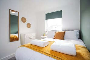 Ein Hotelzimmer mit Bett, Nachttisch, Spiegel und Fenster mit Blick auf Gebäude.