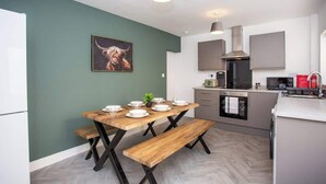A modern kitchen with a dining table, benches, and a microwave. - Vacant nests | The Cowpen | 3BR | Parking & Wi-Fi (Blyth)