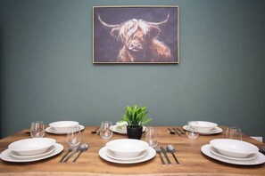 A dining table set with plates, glasses, cutlery, and a potted plant. - Vacant nests | The Cowpen | 3BR | Parking & Wi-Fi (Blyth)