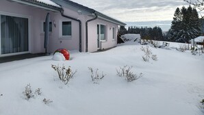 Une maison dont le toit est recouvert de neige, avec une fenêtre bien visible et un amas de neige au premier plan.