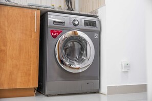 Eine Waschmaschine mit Frontlader in einer Küche mit Holzschrank und weißer Wand.