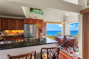 A kitchen with a large island, wooden cabinets, and a view of the ocean. - Pali Ke Kua #231 Serene Ocean Views, Walk to Beach (Princeville)