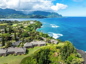 A coastal resort with multiple buildings, a golf course, and a view of the ocean and mountains. - Pali Ke Kua #231 Serene Ocean Views, Walk to Beach (Princeville)