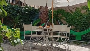 An outdoor patio with a table and chairs under a large umbrella, surrounded by greenery and a hammock. -  30m² studio 90m from the beach in Chania Self Check‑in Parking Garden Fast WiFi (Chania)