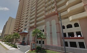 A multi-story hotel with balconies, a sign indicating 'Sunrise Beach Condominium,' and a parking lot with palm trees. - Gulf-Front w/ Balcony Views & Family Comfort Free Golf & Activities Daily! (Panama City Beach)