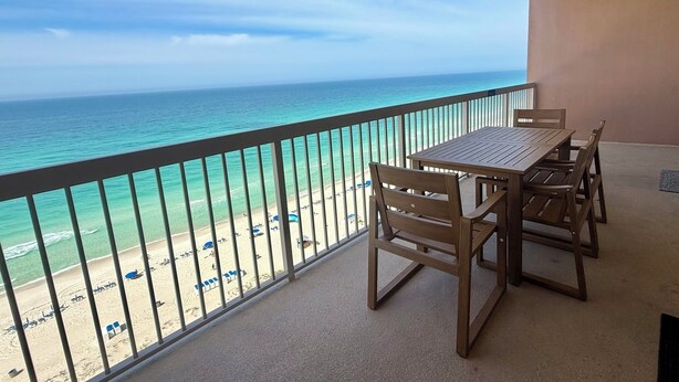 Een balkon met uitzicht op de oceaan en het strand, een houten tafel en stoelen.