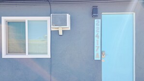 Ein Gebäude mit einer blauen Tür, einem Fenster mit weißem Rahmen und einer Wand-Klimaanlage.