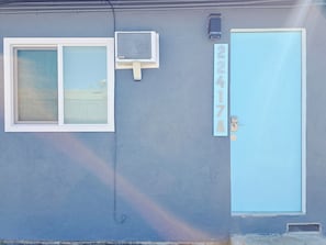 A building with a blue door, a window with a white frame, and a wall-mounted air conditioning unit.