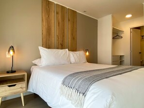 Een slaapkamer met een bed, nachtkastjes, een houten hoofdbord, een hanglamp en een kledingkast.