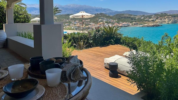 A terrace with a view of a coastal town, a wooden deck, and outdoor seating. - Crete Beachfront Coconut Gem With Seaviews Pool (Apokoronas)