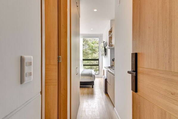 A narrow hallway leading to a bedroom with a bed, a window, and a kitchenette. - w Amazing Loft in the Heart of Chico Norte (Bogotá)